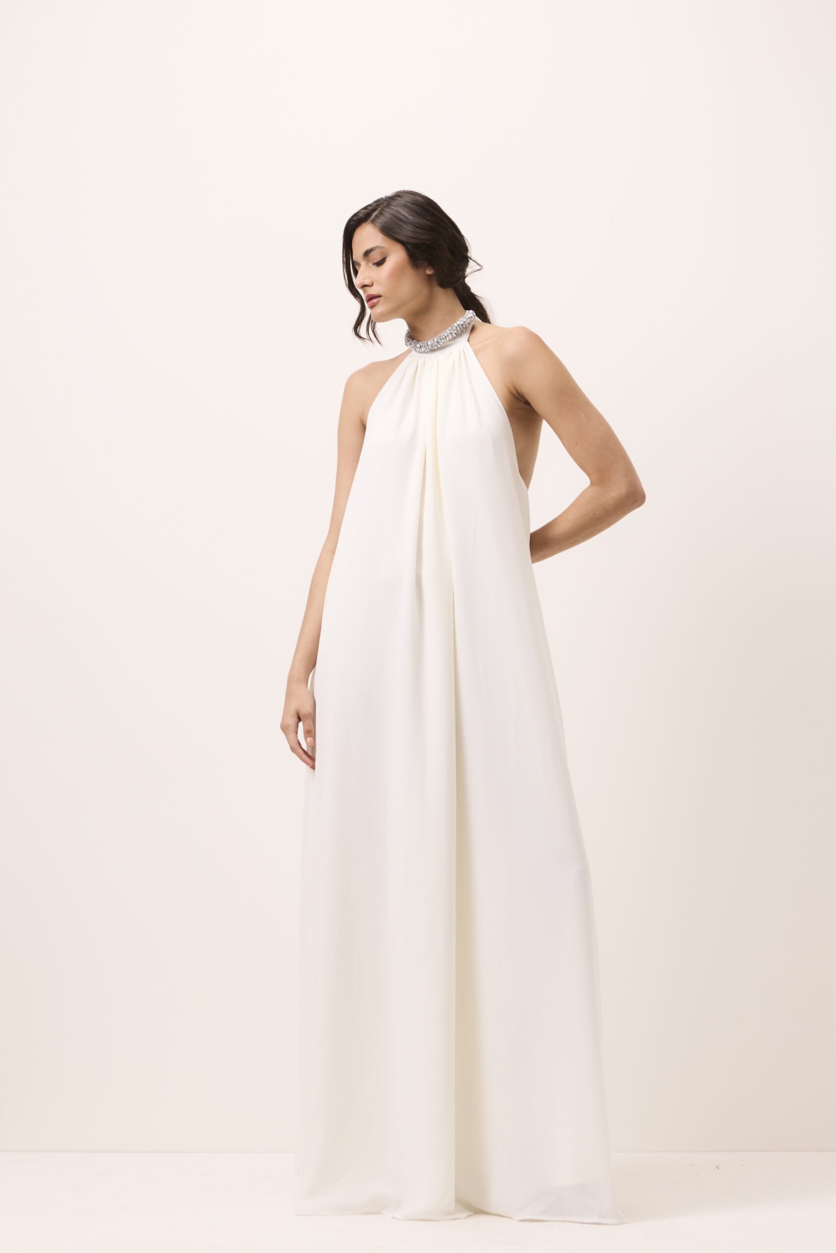 Vestido longo off white em mousseline, frente única halter, gola com laço e colar fixo de cristais, modelagem ampla e decote nas costas